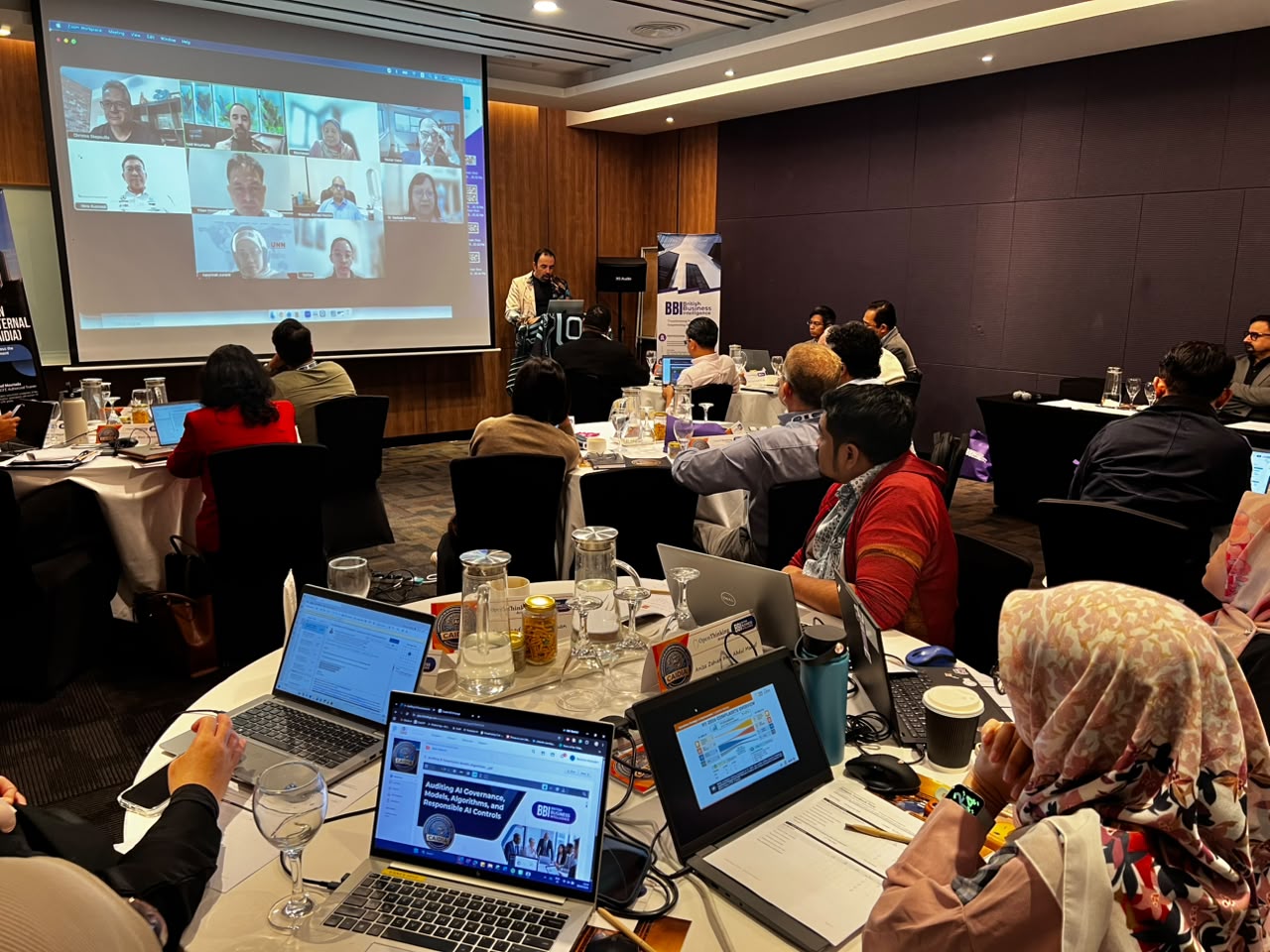 Delegates at round tables with online participants on screen