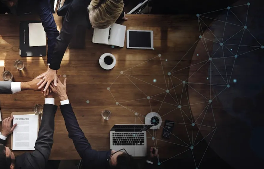 Team joining hands over a meeting table with a digital network overlay